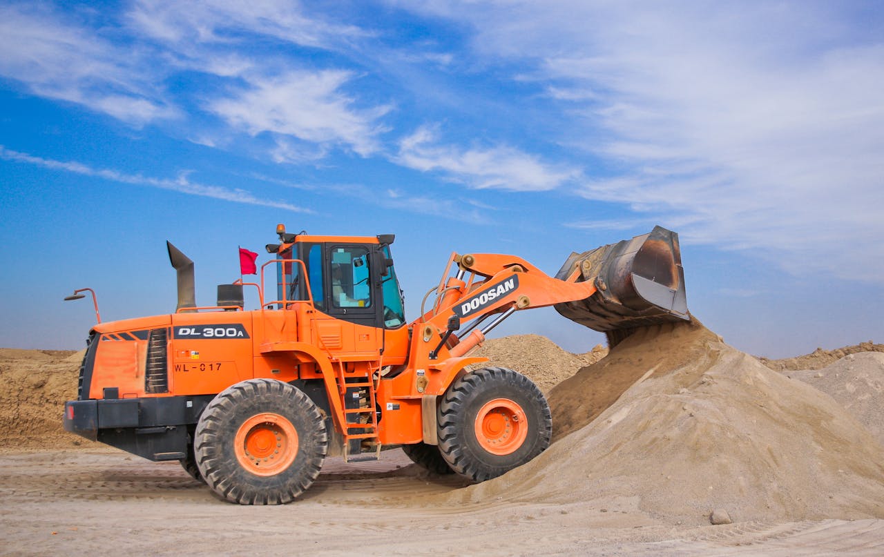 about-02 An orange bulldozer at work, moving sand under a clear blue sky on a construction site.