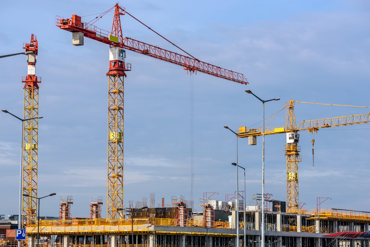 about-01 Multiple tower cranes working on a large construction site with blue sky backdrop.