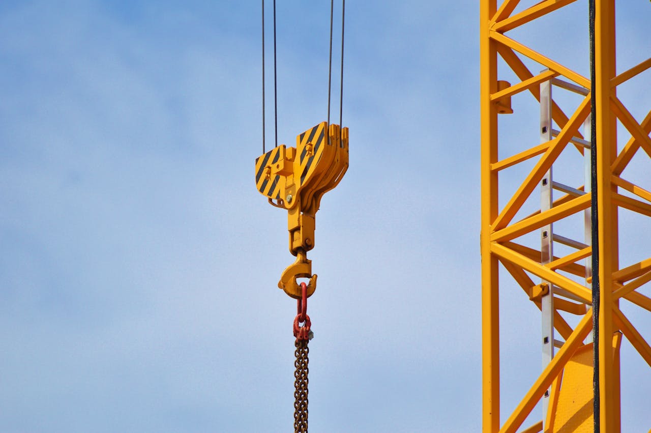 services-01 Close-up of a yellow crane arm against a clear blue sky, showcasing industrial equipment.