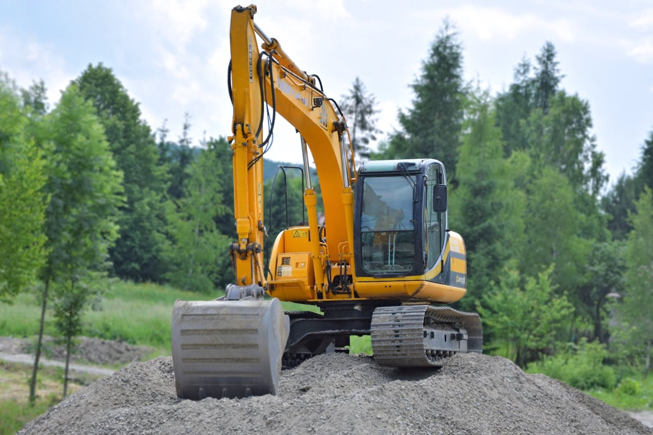 about-03 A yellow excavator on a pile of gravel in a lush, green forest setting in Poland.